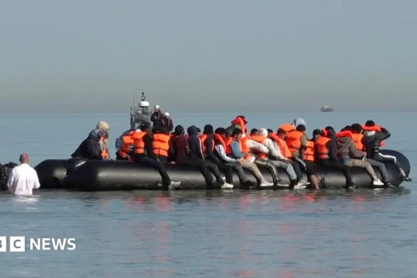 Migrants board a small boat from a beach in northern France during a daytime Channel crossing
